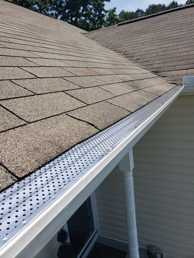Perforated metal gutter guard installed along a shingled roofline